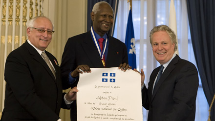 Son Excellence Abdou Diouf, entour du premier ministre, M. Jean Charest, et du prsident du Conseil de l'Ordre, M. Bernard, Voyer, C.Q., prsente firement son brevet sur lequel est crit :  Le gouvernement du Qubec confre  Abdou Diouf le titre de grand officier de l'Ordre national du Qubec en tmoignage de la fiert qu'inspire au peuple du Qubec le mrite exceptionnel de son action. 