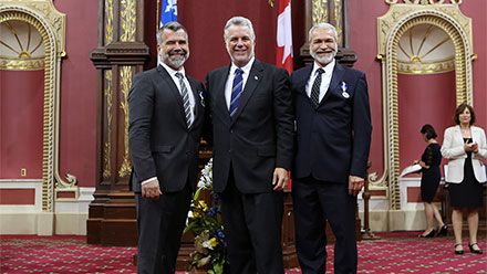 Victor Pilon et Michel Lemieux, nouveaux chevaliers de l’Ordre, entourant le premier ministre. Photo : François Nadeau